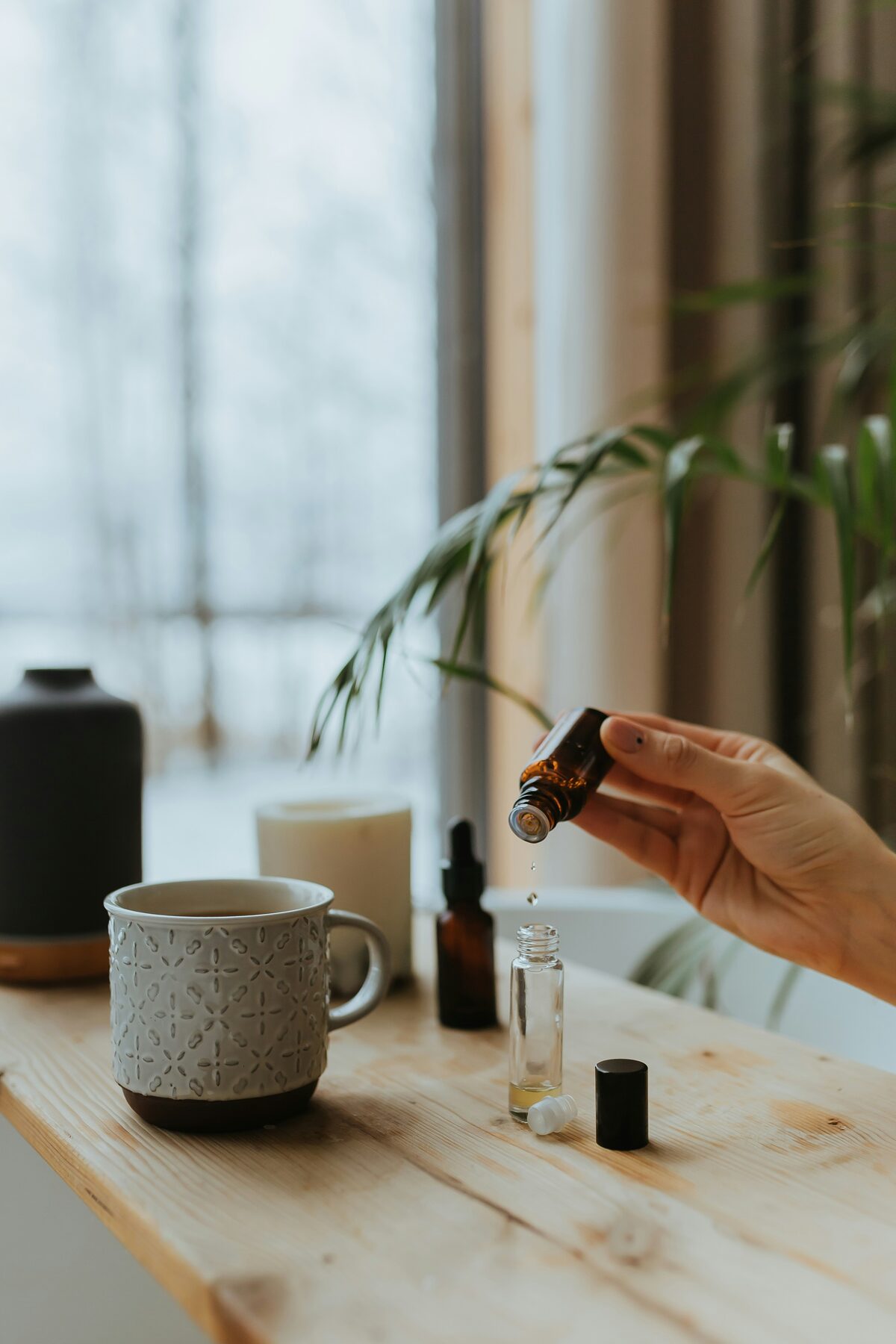 A hand adding drops of Baume Doré to a roller bottle at a sunlit window